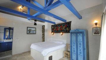 A bedroom with a bed, a blue wardrobe, a wall-mounted tapestry, and a bathroom with a blue cabinet.