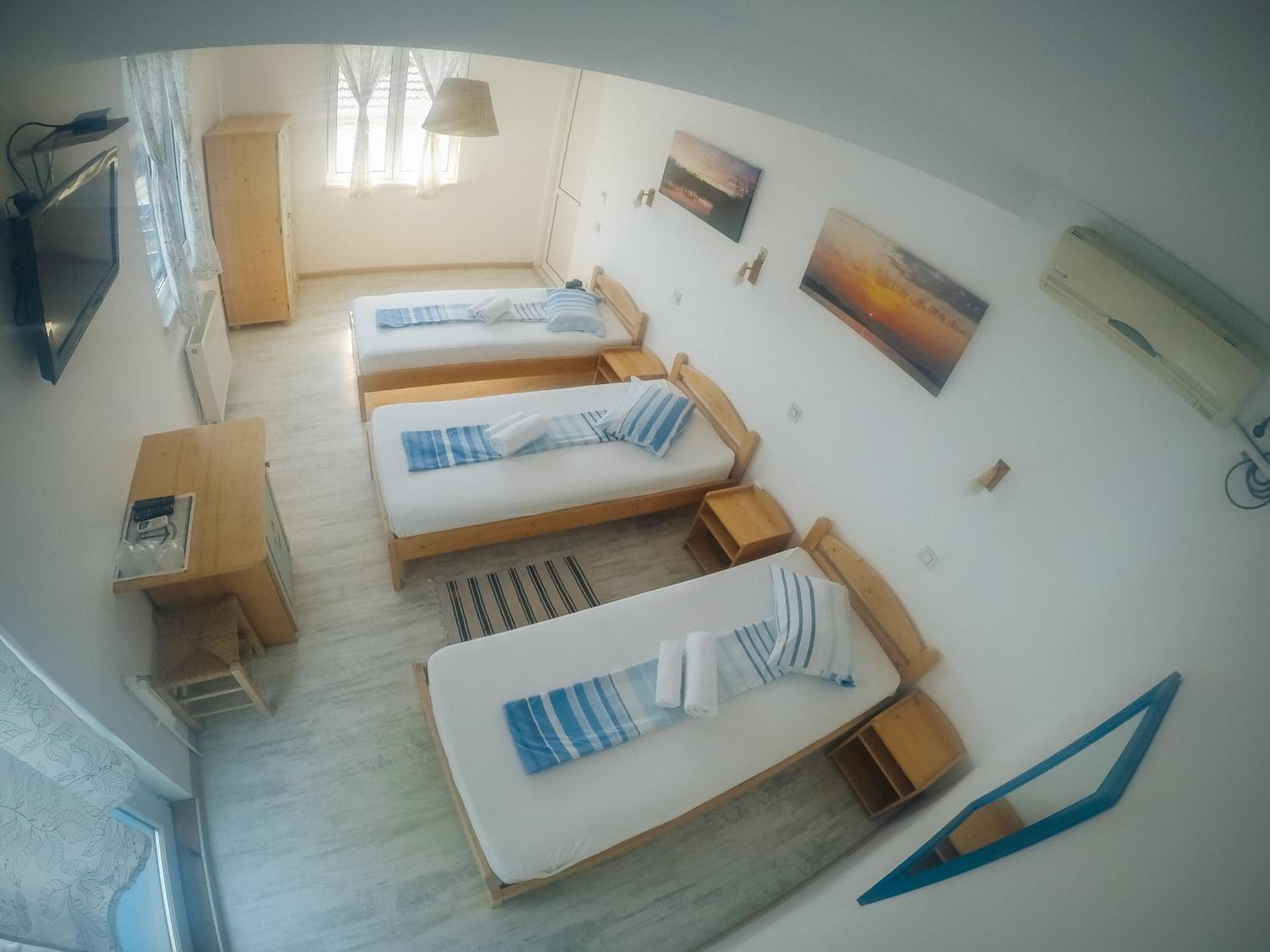 A room with three beds, a desk, a TV, and artwork on the walls.