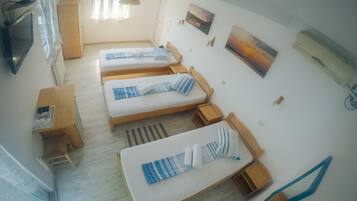 A room with three beds, a desk, a TV, and artwork on the walls.