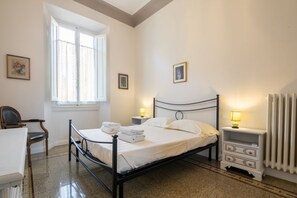 Ein Schlafzimmer mit einem Bett, einem Sessel, einem Nachttisch, einer Lampe, einer Heizung und einem Fenster.