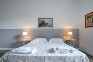 Une chambre d’hôtel avec un lit, deux tables de chevet avec des lampes, un tableau au mur et une photographie encadrée accrochée au mur.