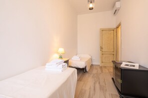 Una habitación pequeña y limpia con dos camas, un escritorio, una lámpara y una puerta.