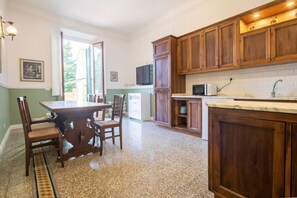 Una cocina con armarios de madera, una mesa de comedor con sillas, un televisor y una ventana con contraventanas.