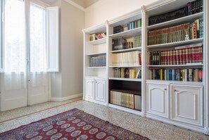 Ein Zimmer mit einem großen Bücherregal, einem gemusterten Teppich und einer Tür mit Vorhängen.