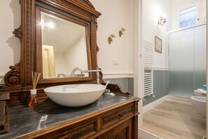 Un baño con un espejo grande, un lavamanos blanco, muebles de madera y una zona de ducha.