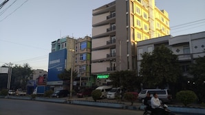 Un edificio de varios pisos con un letrero de Samsung, una señal verde que dice 'PRESENT' y varios vehículos estacionados.