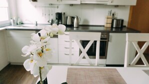 A modern kitchen with white cabinets, a coffee maker, and a dining area with a table and chairs. - Ferienwohnung Worpsweder Schlösschen (Worpswede)