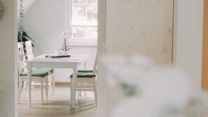 A room with a white table and chairs, a window with a view of trees, and a plant on the table. - Ferienwohnung Worpsweder Schlösschen (Worpswede)