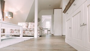 A spacious room with a white sofa, a small table, and a lamp. There is a wooden floor and a white wardrobe in the background. - Ferienwohnung Worpsweder Schlösschen (Worpswede)