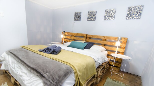 Una cama con cabecera de madera, una mesita de noche y una lámpara de pared.