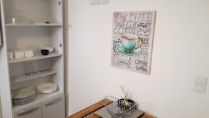 Una cocina con armarios blancos, una mesa de madera y un cuadro con palabras relacionadas al café.
