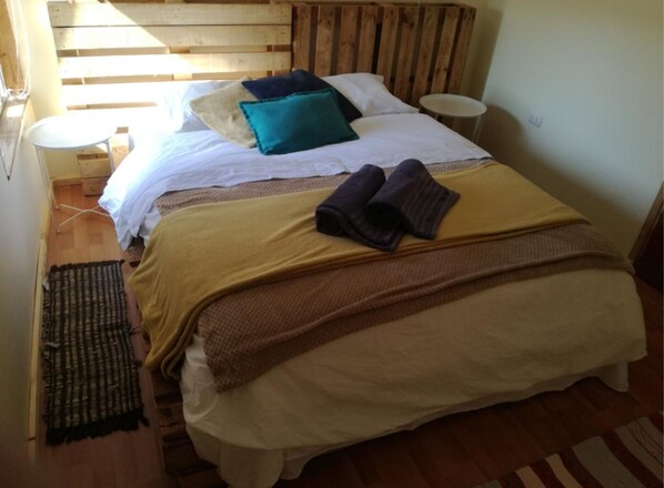 A cozy bedroom with a wooden headboard, a bed with a yellow blanket, a teal pillow, and two folded towels.