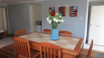 A dining area with a square table, six wooden chairs, and a vase of white flowers.