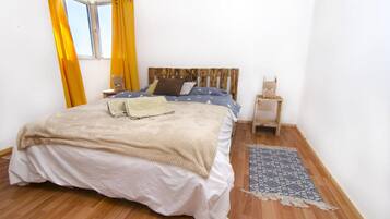 A bedroom with a wooden headboard, a bed with a beige blanket, a nightstand, and a patterned rug.