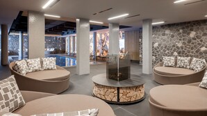 Een moderne lounge met ronde zithoeken, een stenen muur en een zwembad op de achtergrond.