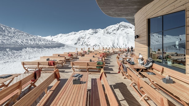 Een houten terras met banken, met uitzicht op een besneeuwd berglandschap.