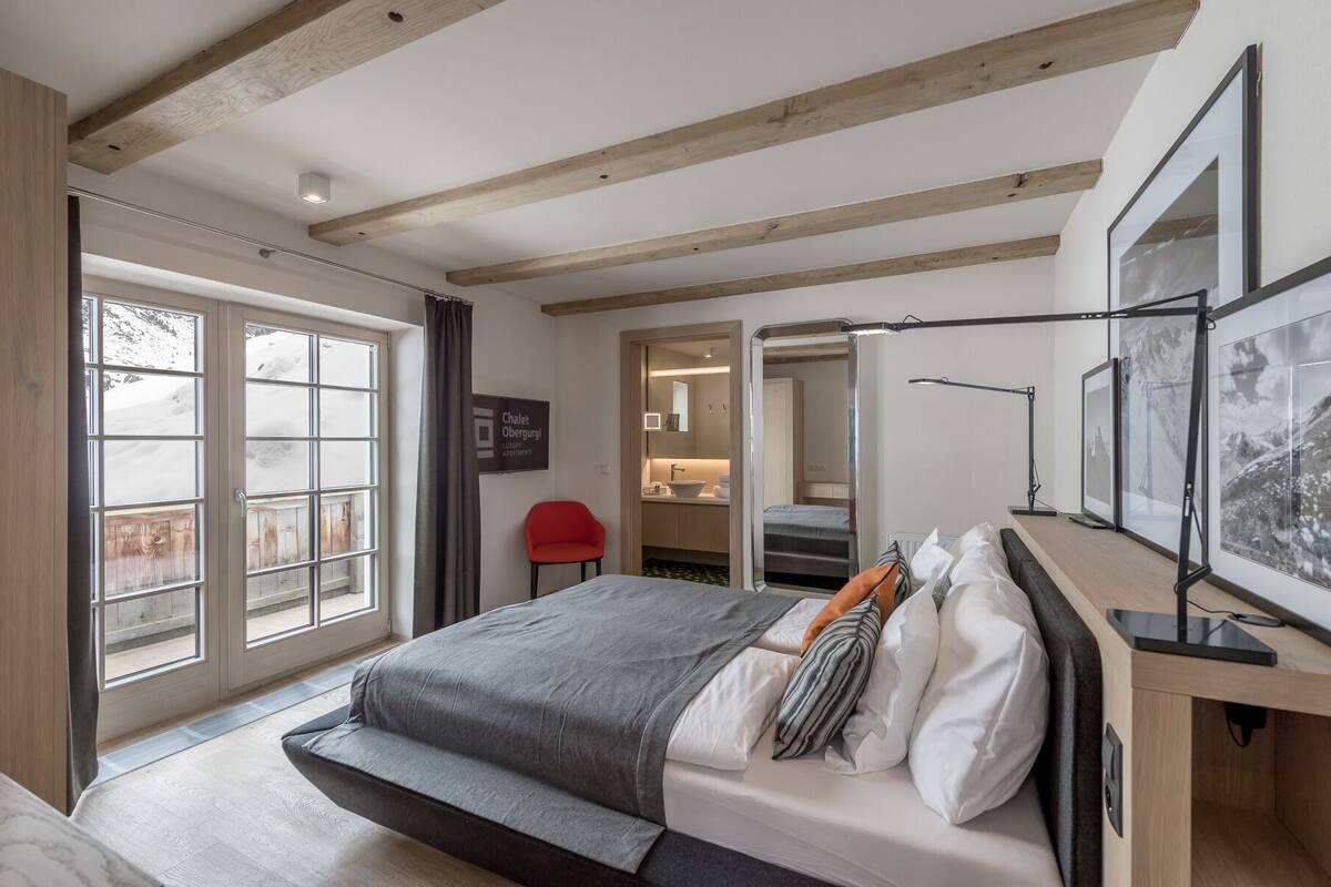 Een slaapkamer met een bed, een bureau, een stoel, een badkamer en uitzicht op de omgeving.