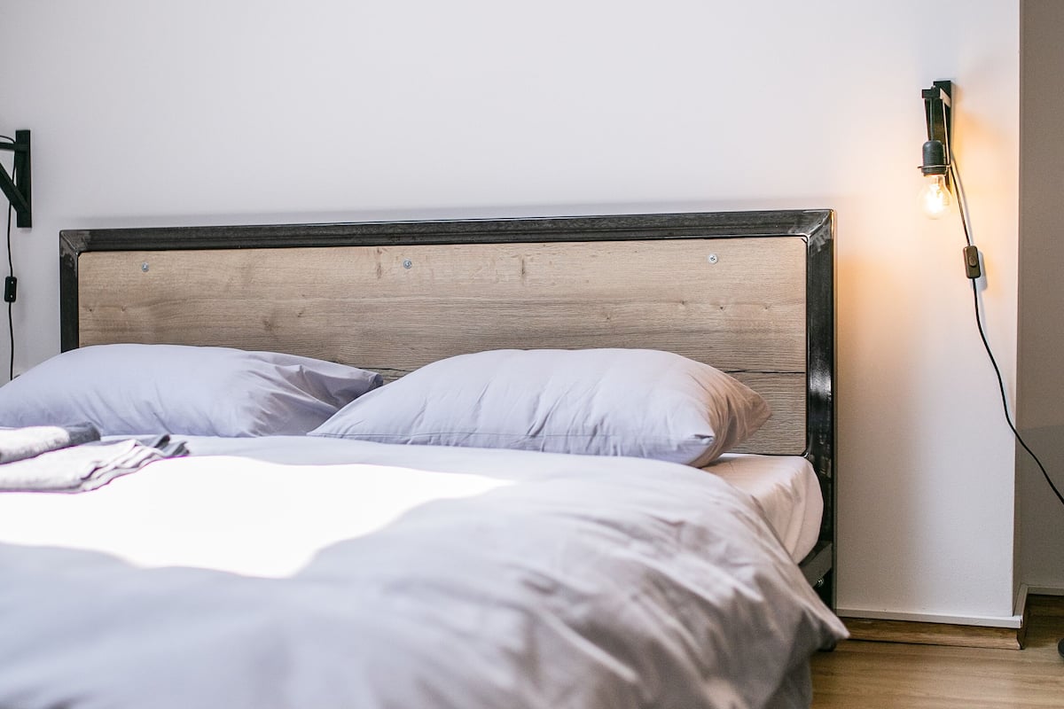 A bed with a wooden headboard, white bedding, and a green rug.