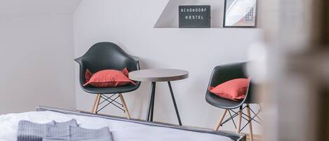 Una habitación de hotel moderna con una cama, dos sillas, una mesita pequeña y un techo inclinado.