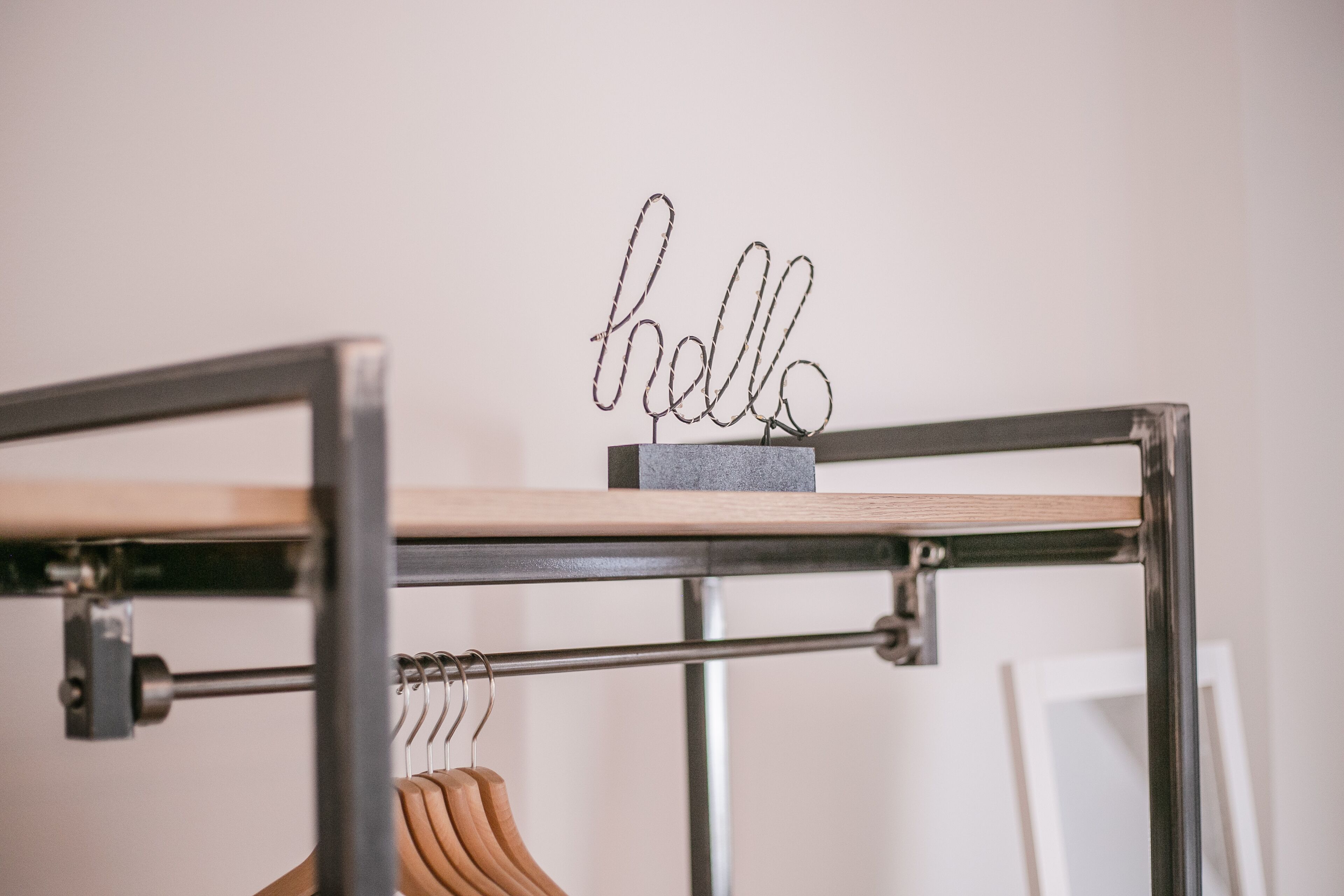 A metal-framed bed with a wooden headboard, a metal shelf with a 'hello' sign, and wooden hangers on a metal rack.