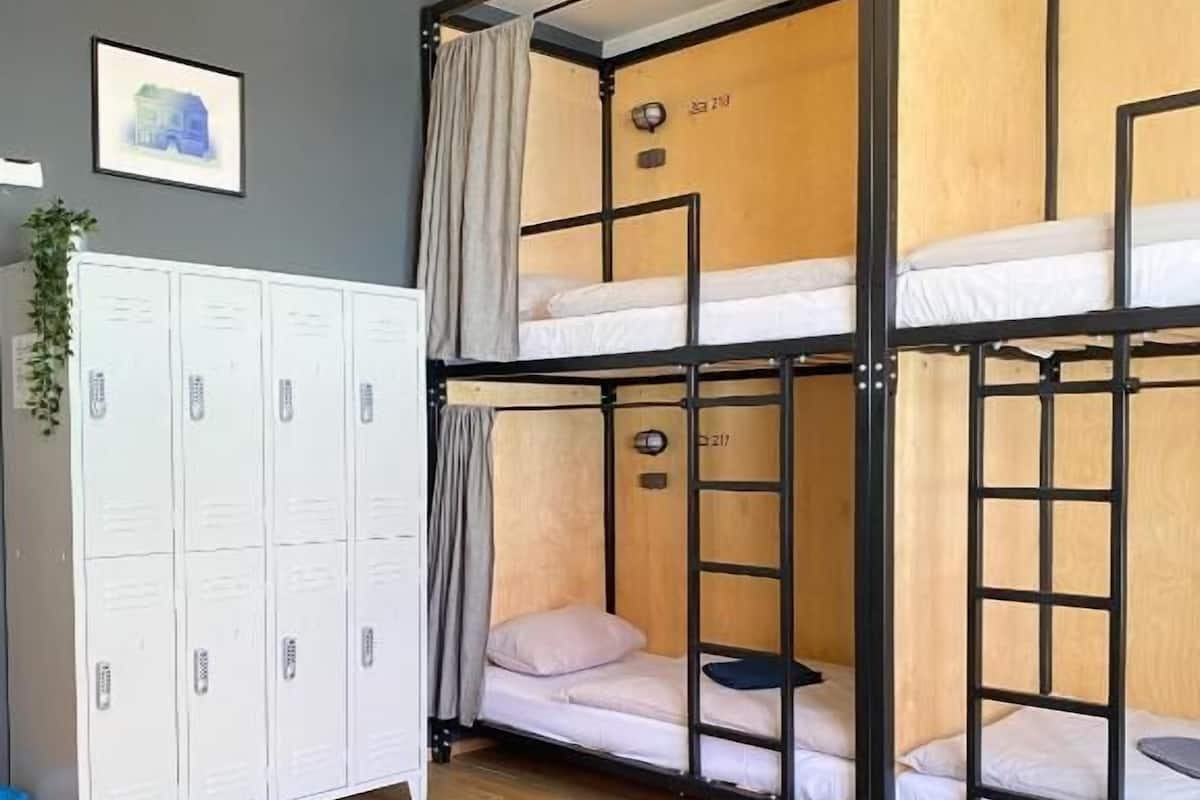 A dormitory room with bunk beds, a white wardrobe, a table, and a hanging light fixture.