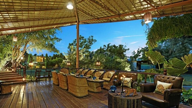 An outdoor seating area with wicker furniture and a leather couch, surrounded by lush greenery and a wooden deck. - The Fern Ranthambhore Forest Resort Sawai Madhopur, Series by Marriott (Sawai Madhopur)