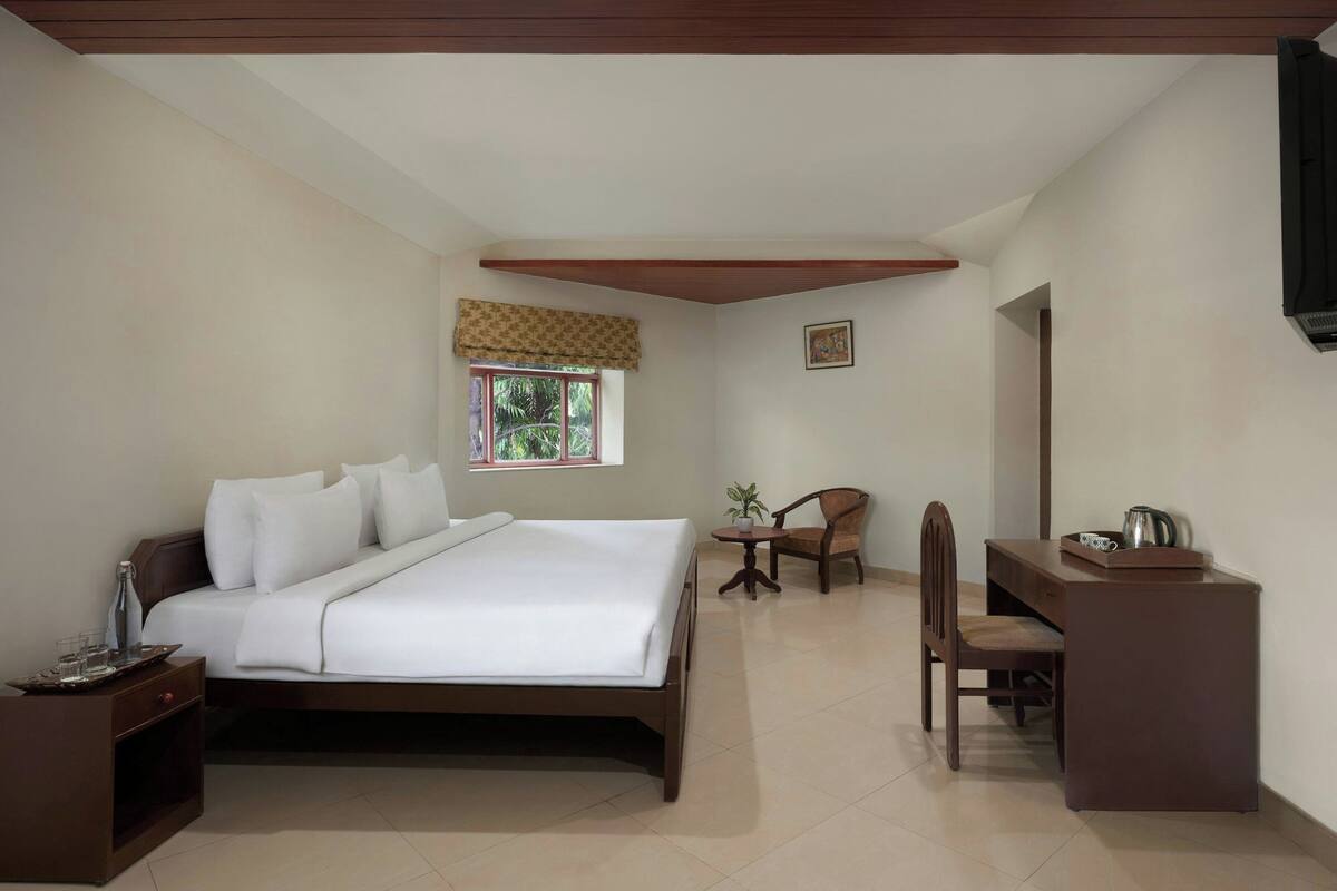 A bedroom with a bed, bedside table, chair, desk, window, and a television.