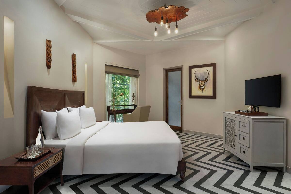 A hotel room with a bed, a TV, a cabinet, and a window with a view of greenery.