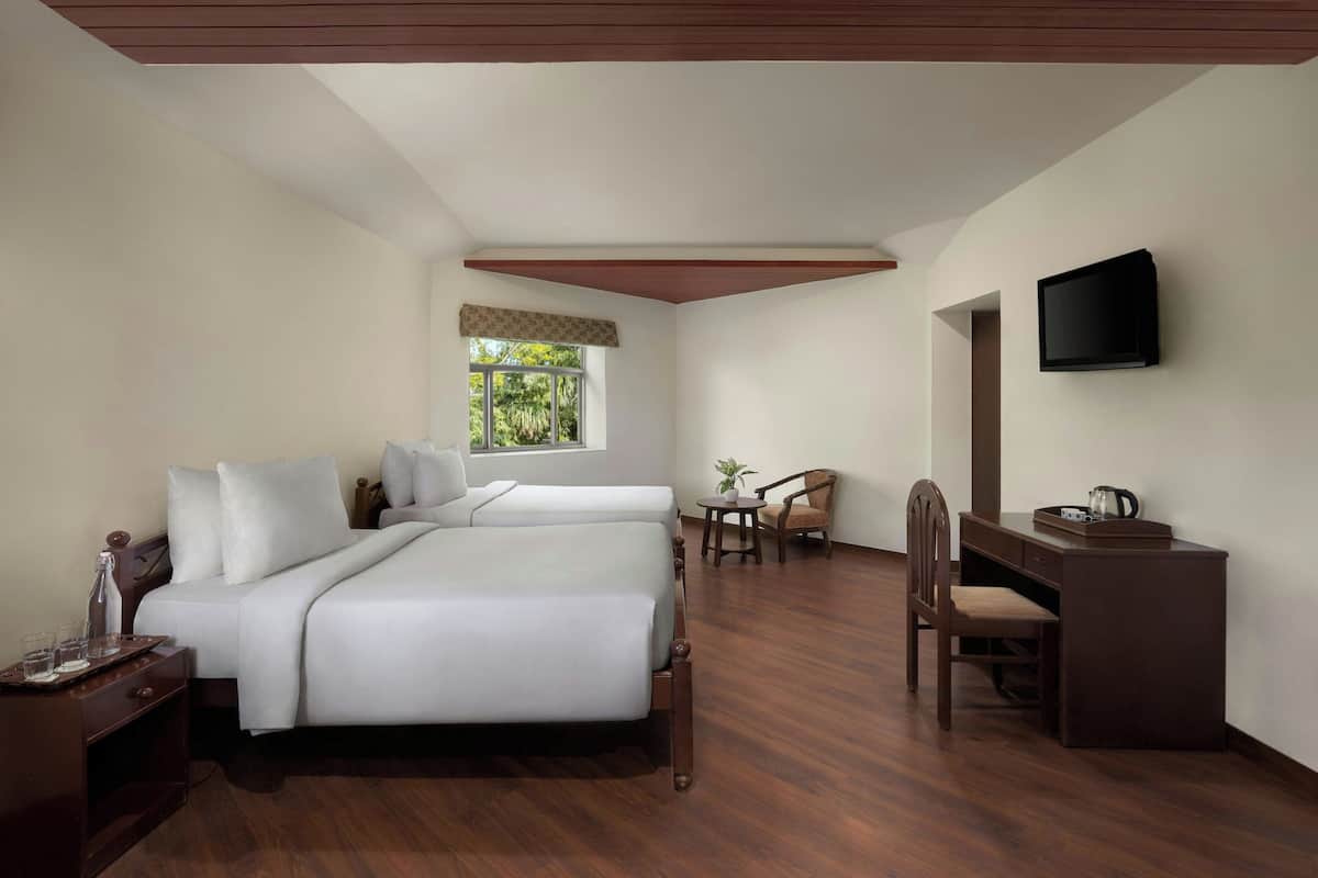 A hotel room with two beds, a desk, a chair, a television, and a window with a view of greenery.