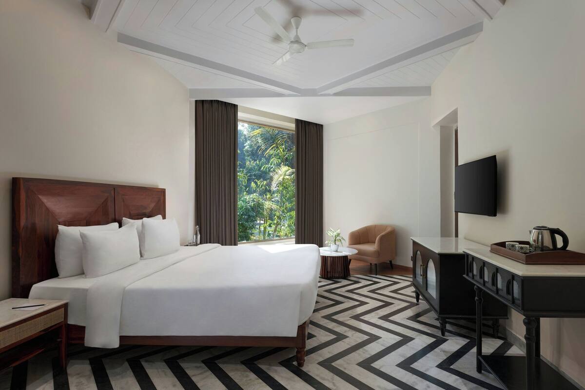 A hotel room with a bed, a desk, a chair, a TV, and a window with curtains.
