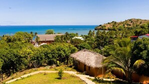 A tropical resort with a thatched-roof building surrounded by lush greenery and a view of the ocean. - Three Bungalows in the sun (NOSY-BE,)