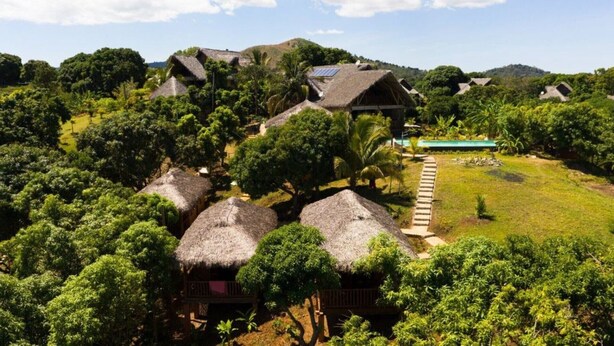 A resort with thatched-roof cottages surrounded by lush greenery and a clear view of a swimming pool. - Three Bungalows in the sun (NOSY-BE,)