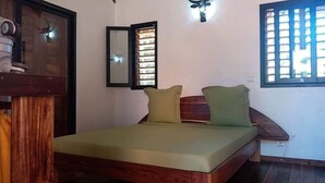 A single bed with a wooden frame and green bedding, a wall-mounted mirror, and a window with vertical blinds. - Three Bungalows in the sun (NOSY-BE,)