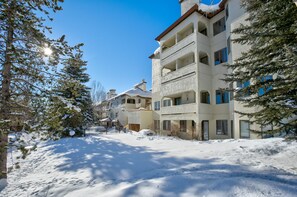 A multi-story building with balconies, surrounded by snow-covered ground and trees.