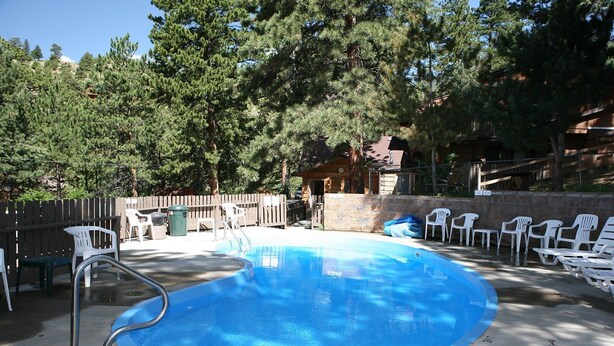 A swimming pool with a diving board, surrounded by white plastic chairs and a wooden fence.