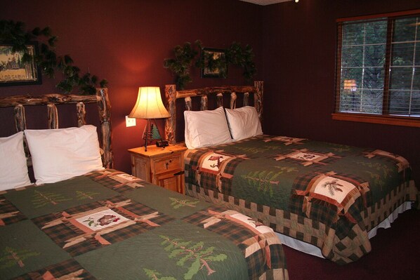 A room with two beds, a nightstand, a lamp, and a window with a view of trees. - Family Sized 1 Bedroom Chalet, sleeps up to 6 (Estes Park)