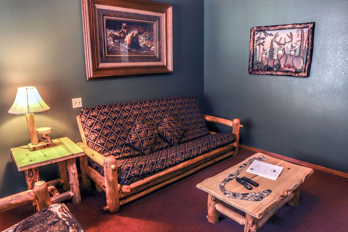 A cozy room with a wooden sofa, a small wooden table with a remote control, a lamp, and framed pictures on the wall.