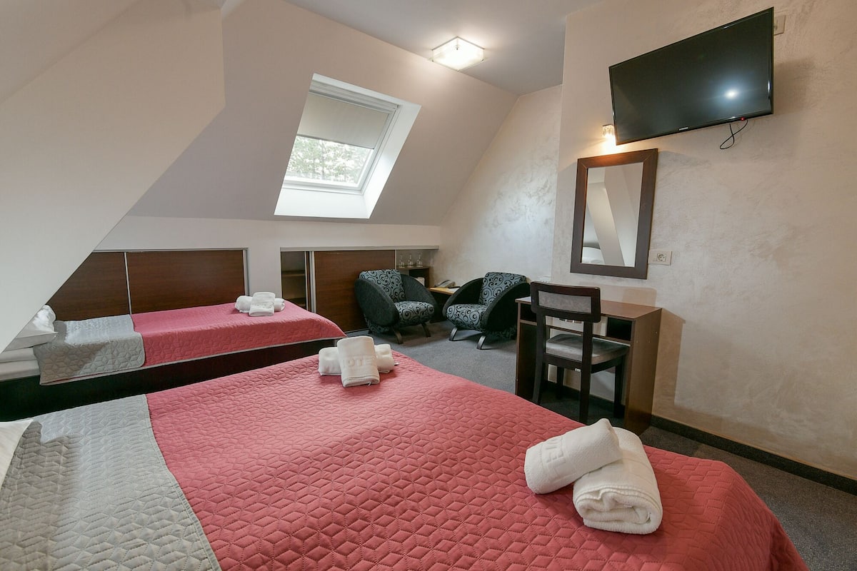 A hotel room with two beds, a TV, a desk, and a window.