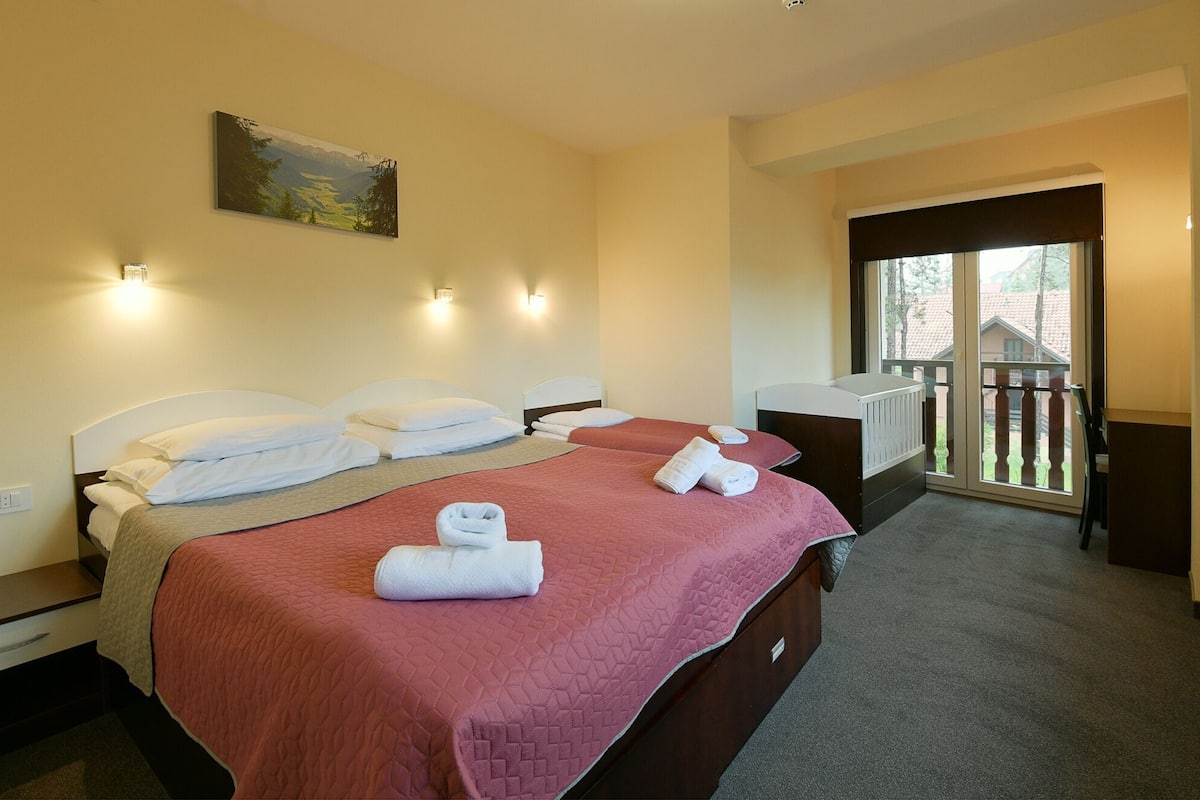 A hotel room with two beds, a painting on the wall, and a balcony with a view.
