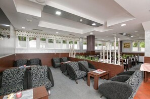 A restaurant with a modern interior, featuring patterned sofas, wooden tables, and a view of the outdoors through large windows. - Hotel Simsir (Zlatibor)