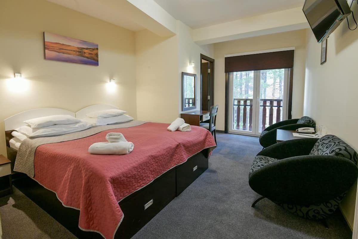 A bedroom with a bed, a desk, a chair, and a balcony.