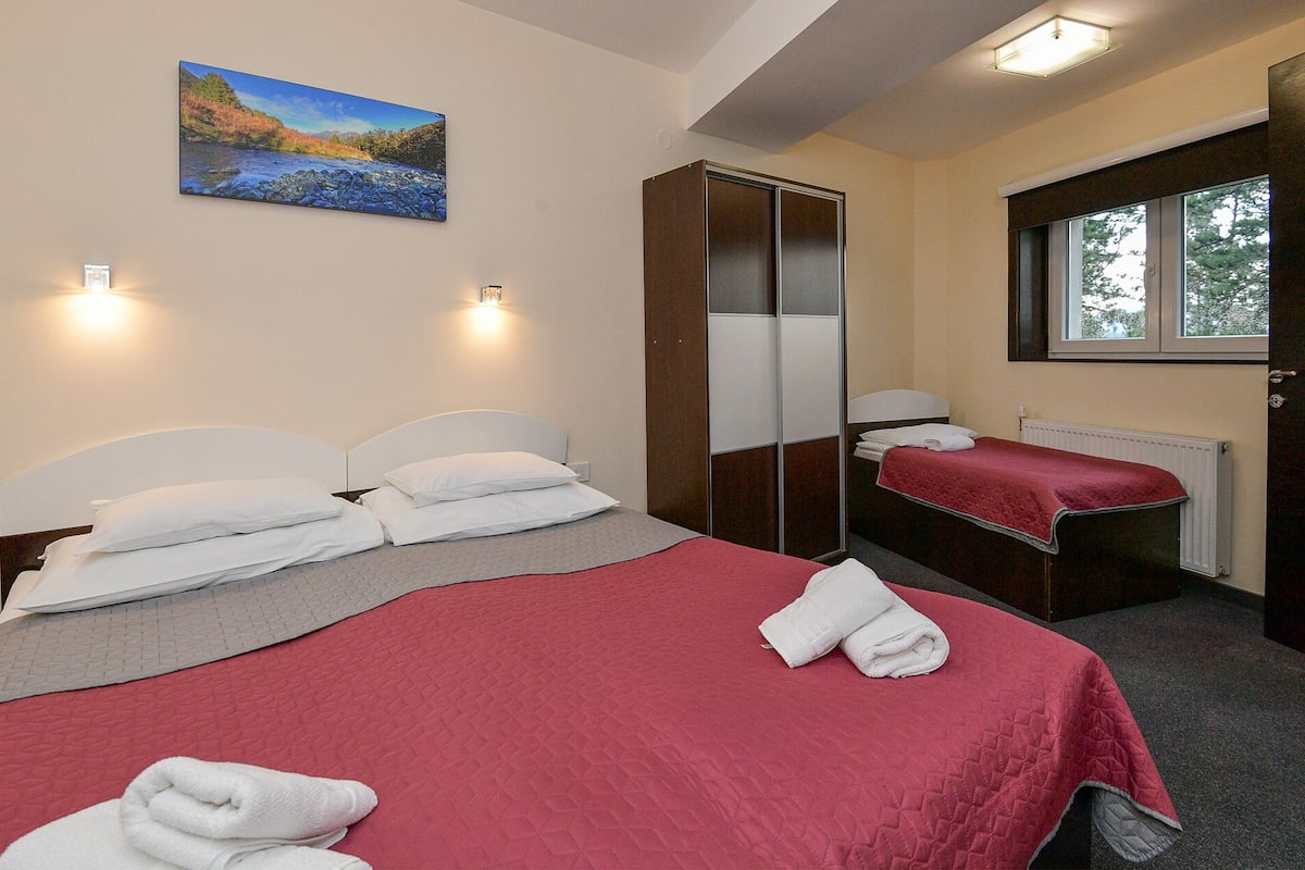 A hotel room with two beds, a large mirror, a window, and a painting on the wall.