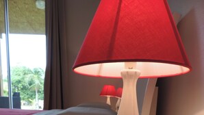 A white bedside table with a white lamp featuring a red lampshade. - Villa Manapany les bains 2 (Manapany-Les-Bains)