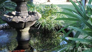 A stone fountain with multiple tiers, surrounded by lush greenery and palm trees. - Villa Manapany les bains 2 (Manapany-Les-Bains)