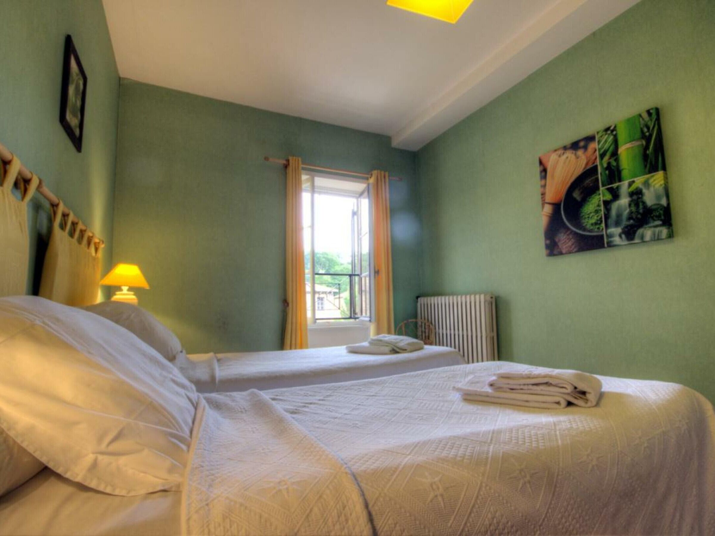 A hotel room with two beds, a window with curtains, a radiator, and a painting on the wall.