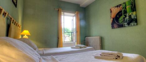 A hotel room with two beds, a window with curtains, a radiator, and a painting on the wall.