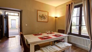 Un comedor con una mesa lista para dos personas, un banco, un cuadro en la pared y una ventana con cortinas.
