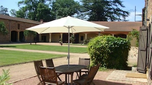 Un patio al aire libre con una mesa, sillas, un parasol grande y un edificio de ladrillo al fondo.