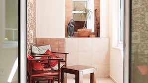 Habitación de esquina con un banco de madera, una silla, una mesita y una planta en maceta.