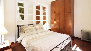 Un dormitorio con cama, armario, ventana con cortinas y radiador.